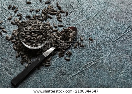 Bowl and spoon with black sunflower seeds on dark background