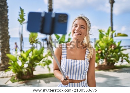 Young blonde girl smiling happy making selfie by the smartphone at the promenade.