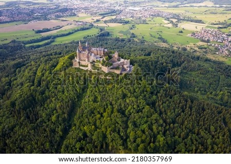 Drone shot of Hohenzollern Castle on forested mountain top in the Swabian Alps in summer. Scenic aerial view of old German Burg. Famous fairytale Gothic landmark in Stuttgart vicinity Royalty-Free Stock Photo #2180357969
