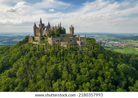 Drone shot of Hohenzollern Castle on forested mountain top in the Swabian Alps in summer. Scenic aerial view of old German Burg. Famous fairytale Gothic landmark in Stuttgart vicinity Royalty-Free Stock Photo #2180357993