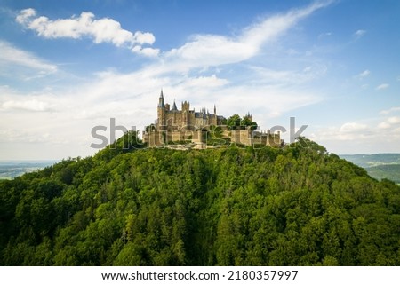 Drone shot of Hohenzollern Castle on forested mountain top in the Swabian Alps in summer. Scenic aerial view of old German Burg. Famous fairytale Gothic landmark in Stuttgart vicinity Royalty-Free Stock Photo #2180357997