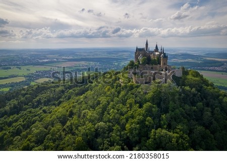 Drone shot of Hohenzollern Castle on forested mountain top in the Swabian Alps in summer. Scenic aerial view of old German Burg. Famous fairytale Gothic landmark in Stuttgart vicinity Royalty-Free Stock Photo #2180358015