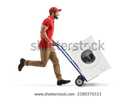 Full length profile shot of a male worker running and pushing a hand-truck with a washing machine isolated on white background