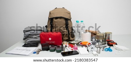 Emergency backpack equipment organized on the table. Documents, water,food, first aid kit and another items needed to survive. Royalty-Free Stock Photo #2180383547