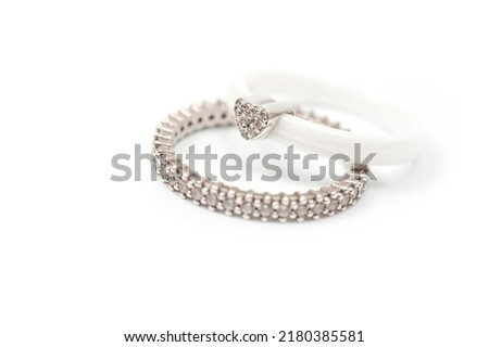 A white ceramic ring with a metal heart decorated with rhinestones and a silver ring with decorative stones.