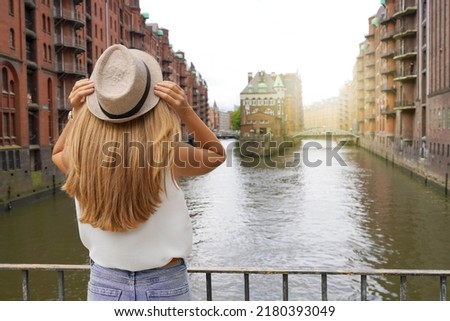 Tourism in Germany. Beautiful young woman visiting Speicherstadt district in the port of Hamburg, Germany. UNESCO World Heritage Site. Royalty-Free Stock Photo #2180393049