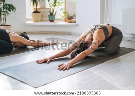 Young fit women practice yoga doing asana in bright yoga studio. Yoga ticher practice with student in yoga class Royalty-Free Stock Photo #2180393305