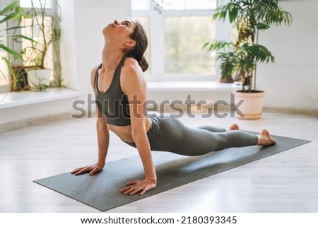 Young fit woman practice yoga doing asana in light yoga studio with green house plant Royalty-Free Stock Photo #2180393345