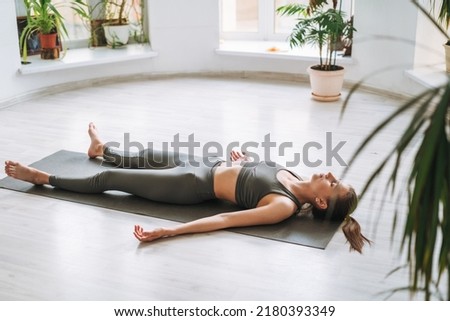 Young fit woman practice yoga doing savasana in light yoga studio with green house plant Royalty-Free Stock Photo #2180393349