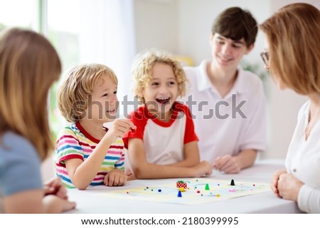 Family playing board game at home. Kids play strategic game. Little boy throwing dice. Fun indoor activity for summer vacation. Siblings bond. Educational toys. Friends enjoy game night. Royalty-Free Stock Photo #2180399995