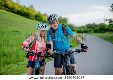Active senior couple resting after bicycle ride at summer park, using smartphone. Royalty-Free Stock Photo #2180402057