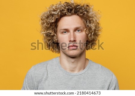 Young cute calm cool blond caucasian european serious attractive man 20s he wearing basic grey t-shirt looking camera isolated on plain yellow color background studio portrait. People lifestyle concept