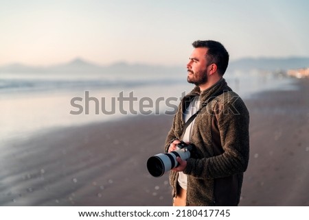 happy latin photographer holding professional camera on the beach looking at the horizon