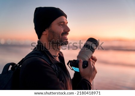 latin mature photographer holding professional camera on the beach and smiling happy portrait Royalty-Free Stock Photo #2180418971