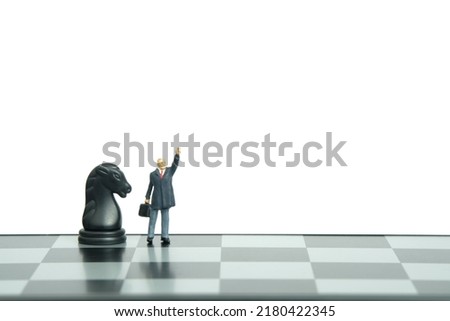 Miniature people toy figure photography. Power up strategy concept. A businessman standing beside horse knight pawn on chessboard while raise his hand. Isolated on white background. Image photo