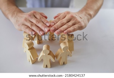Man holding hands over small wooden pawn people, close up. Responsible team manager protects employees, guards their interests and creates safe working environment. Community, corporate safety concept