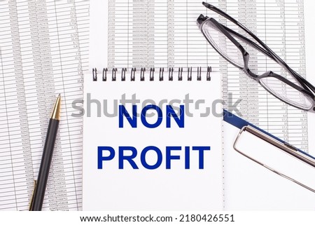 A white notepad with the text NON PROFIT, a pen, reports and glasses lie on a white office table. View from above