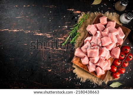 Pieces of raw pork on a wooden plate with spices and tomatoes. On a black background. High quality photo