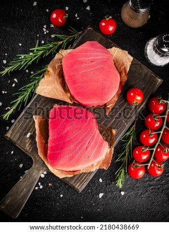 Raw tuna on a cutting board with tomatoes and rosemary. On a black background. High quality photo