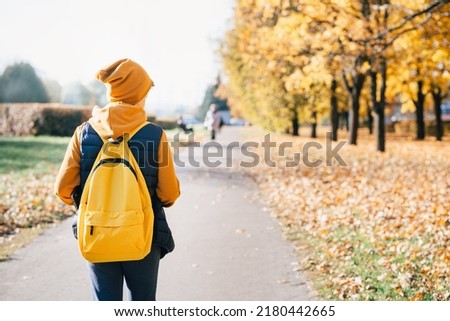 Child caucasian teen boy in yellow beany hat and backpack walking outdoors with laptop. Fall autumn. Remote or distant learning on the go. Back to school. Homeschooling. Video call. Copy space.