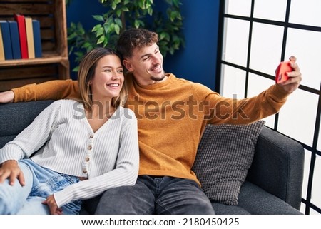 Young man and woman couple make selfie by the smartphone sitting on sofa at home