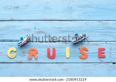 Colorful letters and decorative boats laid out in the word "Cruise" on blue wooden background.