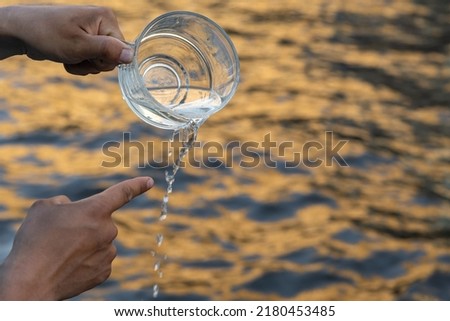 The hand holds a mug from which water is poured out and the other hand points to the jet. Background picture. Space for printing text.