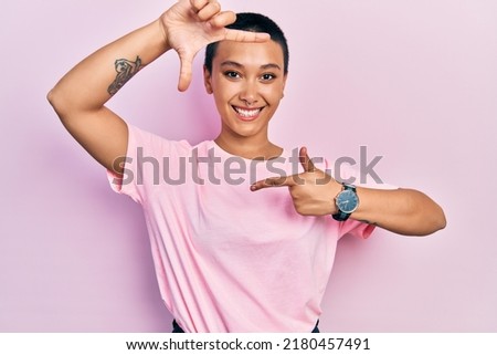 Beautiful hispanic woman with short hair wearing casual pink t shirt smiling making frame with hands and fingers with happy face. creativity and photography concept. 