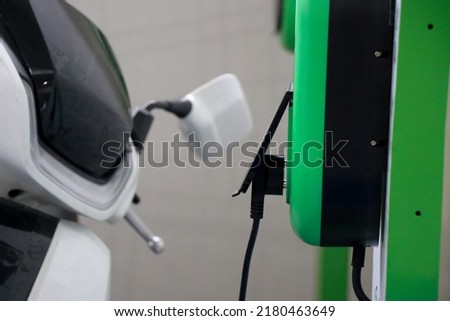Electric scooter plugged to charging point with a view of the scooter in the background Royalty-Free Stock Photo #2180463649