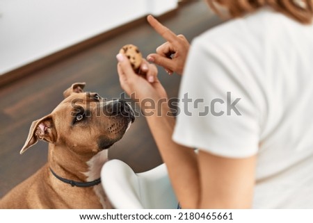 Young caucasian woman teaching dog prohibition eat cookies at home Royalty-Free Stock Photo #2180465661