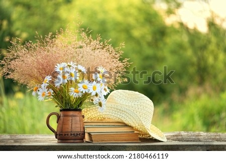 flowers Bouquet, old books and braided hat on table in garden, abstract natural background. Harmony, peaceful, relax mood. summer season concept. Rustic composition with flowers. template for design Royalty-Free Stock Photo #2180466119
