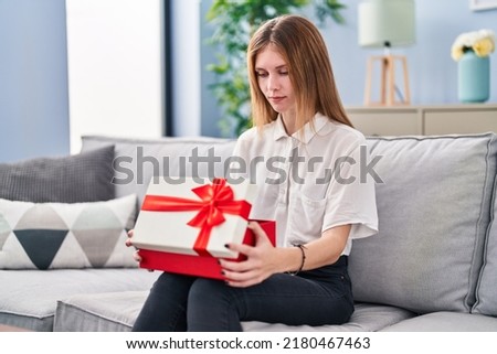 Beautiful woman holding gift relaxed with serious expression on face. simple and natural looking at the camera. 