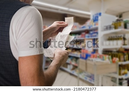 Closeup of young man holding bill to check the price in supermarket Royalty-Free Stock Photo #2180472377
