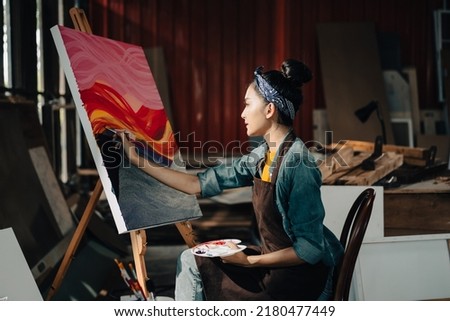 Asian Female Artist Draws create art piece with palette and brush painting at studio.