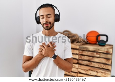 African american man listening to music using headphones at the gym smiling with hands on chest with closed eyes and grateful gesture on face. health concept. 
