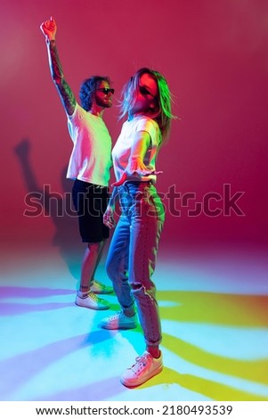 Portrait of young stylish man and woman dancing, posing isolated over red background in neon light. Dancing. Feeling good. Concept of youth, lifestyle, relationship, emotions, facial expression, ad