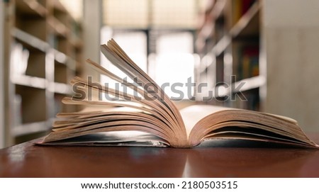 An open book or textbook in the library with light from the window on the reading table and the corridor of the bookshelves in the school classroom background.Education learning concept