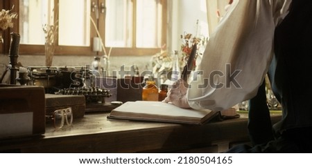 A man writer dips his pen into an inkwell and prepares to write a book in his workshop. Cosplay of the Middle Ages. Cinematic concept. Close-up feather