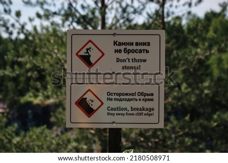 Ruskeala Mountain Park, Karelia. Sign in Russian and English warns of danger. Not to approach edge of cliff, don't throw stones down. Red rhombus on white background and silhouette of man on mountain.