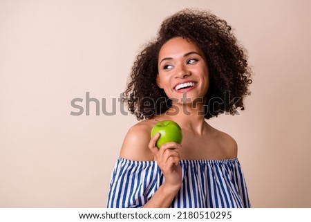Photo of dreamy sweet girl dressed off shoulders clothes eating green apple looking empty space isolated beige color background
