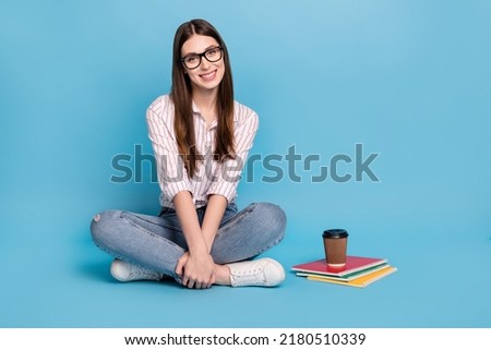 Portrait of beautiful trendy cheerful smart girl sitting doing home task isolated over bright blue color background
