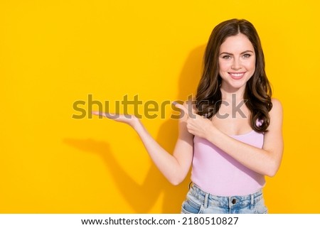 Portrait of cheerful girl indicate finger hands hold empty space proposition isolated on yellow color background