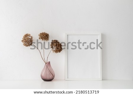 Picture frame and minimal vase with a decorative dried branches, flower against white wall.	
