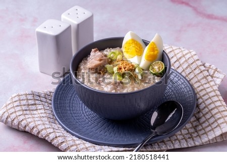 Arroz caldo, is a Filipino rice and chicken gruel heavily infused with ginger and garnished with toasted garlic, scallions, and black pepper. It is usually served with calamansi or fish sauce (patis)  Royalty-Free Stock Photo #2180518441