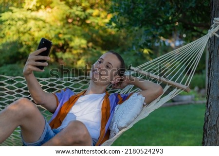 Young handsome man taking a selfie while laying in a hammock in the afternoon in summer time