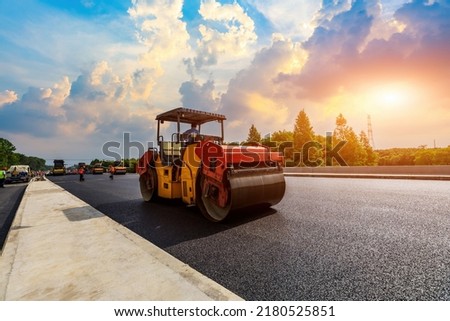 Construction site is laying new asphalt pavement, road construction workers and road construction machinery scene.  Royalty-Free Stock Photo #2180525851
