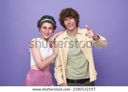 portrait of happy excited couple tourists pointing hands to front on isolated light purple background.