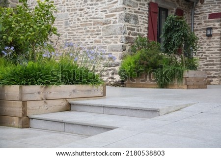 Modern garden and terrace design: Hillside plot paved with natural flagstones in contrast to raised beds planted with plants, lemon tree, agapanthus in wooden pots in front of an old stone wall Royalty-Free Stock Photo #2180538803