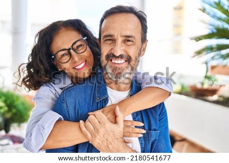 Middle age hispanic couple smiling confident hugging each other sitting on hammock at terrace Royalty-Free Stock Photo #2180541677