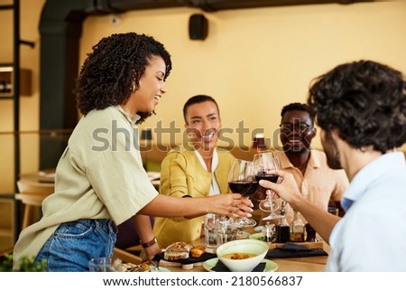 Interracial friends are toasting for success in a restaurant with red wine.